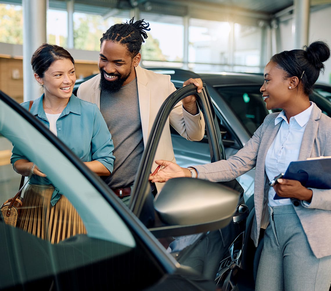 A man and woman examine a car together at a dealership.